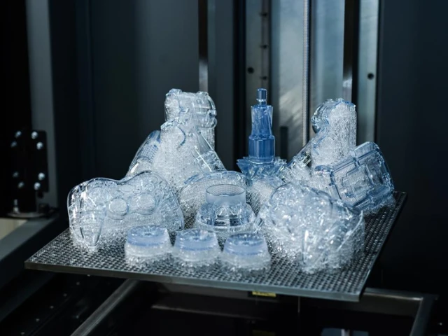 Mehrere verschiedene 3D-gedruckte transparente Bauteile auf einer Bauplatte, die mit dem Resin 3D-Druck und der SLA-Technologie (Stereolithografie) hergestellt wurden.